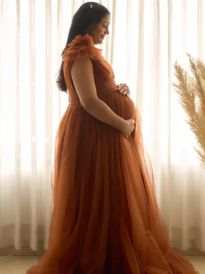A silhouette shot of the Copper gown. The flowing tulle fabric is beautifully backlit, highlighting the shape of the baby bump.
