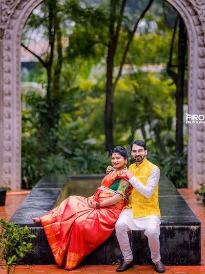 This couple chose a beautiful red and green silk saree for their traditional maternity shoot. The rich colors and classic attire look stunning against the natural backdrop of the stone archway and greenery.