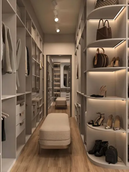 A long, galley-style walk-in closet with curved shelving for shoes and bags. The bright, even lighting and central bench create a high-end, boutique-like experience.