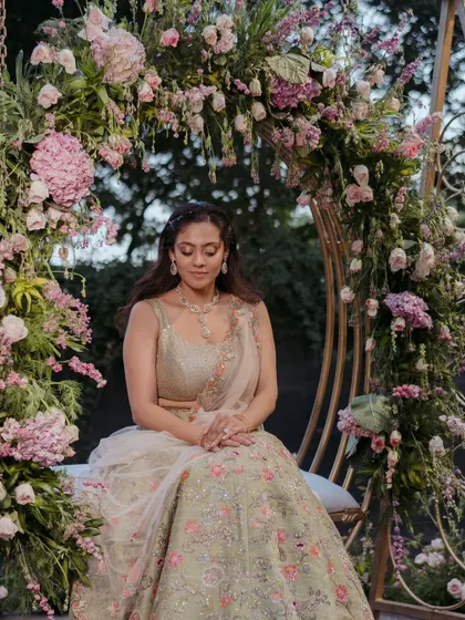 The bride seated on a floral swing at her Mehendi sundowner. The arch of pink flowers perfectly frames her, creating a picturesque moment of tranquility before the festivities.