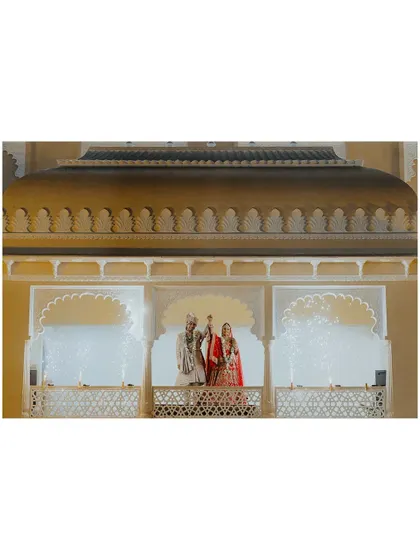 A wide shot of the couple on the palace balcony. This image captures the scale and beauty of their destination wedding venue, creating a truly cinematic and unforgettable portrait.