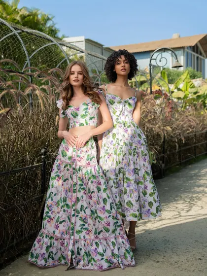 An outdoor campaign image for fashion brand Tangerine Tiger. This shot features two models in complementary floral outfits, set in a lush garden to evoke a fresh, summery feel.