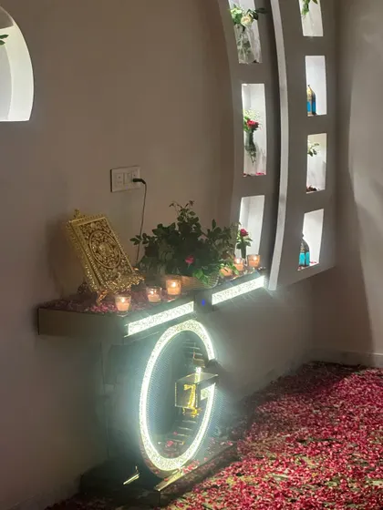 A personalized corner in the 'Welcome Bride' room, featuring an illuminated initial 'G', a holy book on a stand, and a console table decorated with flowers and candles.