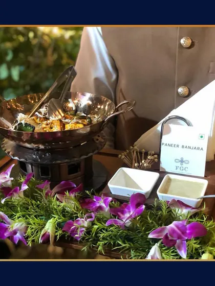 A close-up of the Paneer Banjara being served. The vibrant colors of the dish and the purple orchids create a visually appealing composition that speaks to our brand of luxury.