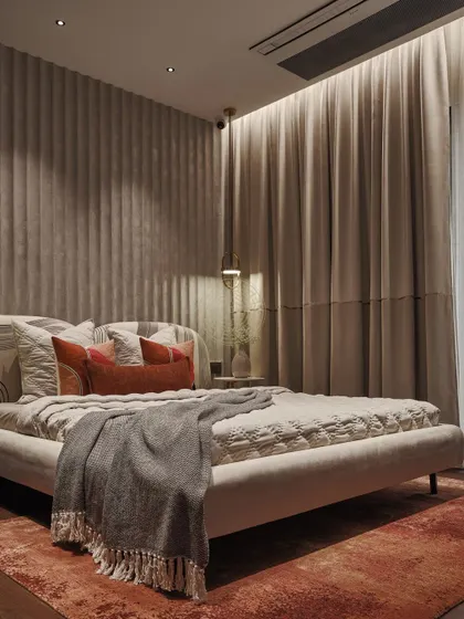 Warm tones create an inviting atmosphere in this second bedroom. A fully upholstered bed is set against a fabric-paneled wall, with a rust-colored rug and throw pillows adding a pop of color.