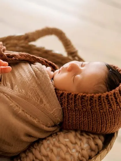 This portrait highlights a cozy knit bonnet and a matching wrap. The textures of the woven basket and soft fabrics add depth and warmth to the image.