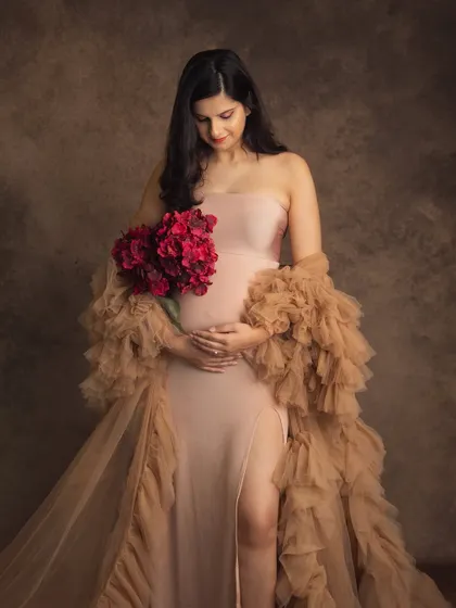 Holding a bouquet of deep red flowers adds a beautiful pop of color and a touch of romance to this elegant studio maternity portrait.