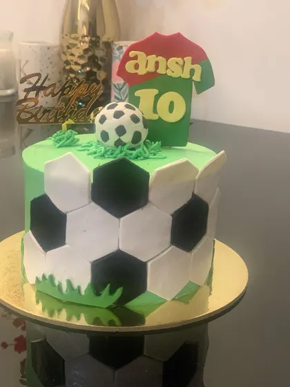 A simple and fun football cake. The design features a soccer ball pattern, a jersey with the birthday boy's name and age, and a ball on top.