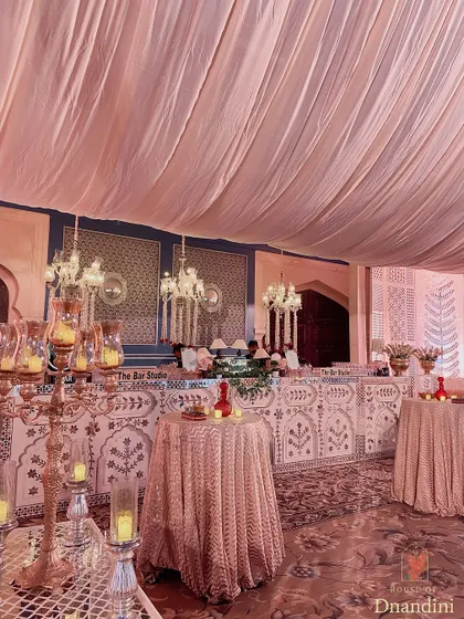 The bar area, with a custom-made front featuring traditional Rajasthani motifs. The space is softened with fabric draping and illuminated by elegant chandeliers.