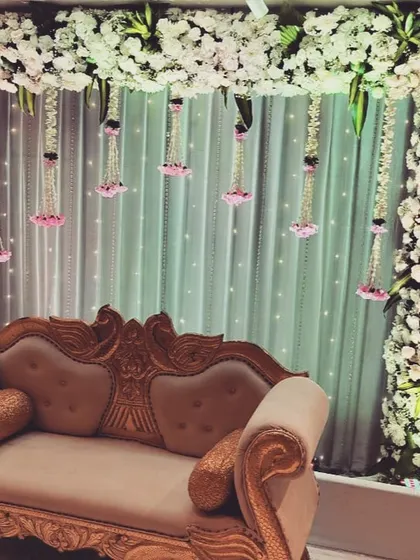 A simple and elegant seating area for an intimate Roka or Gor Dhana ceremony. The backdrop of white flowers and hanging pink floral strings provides a beautiful setting for small gatherings.