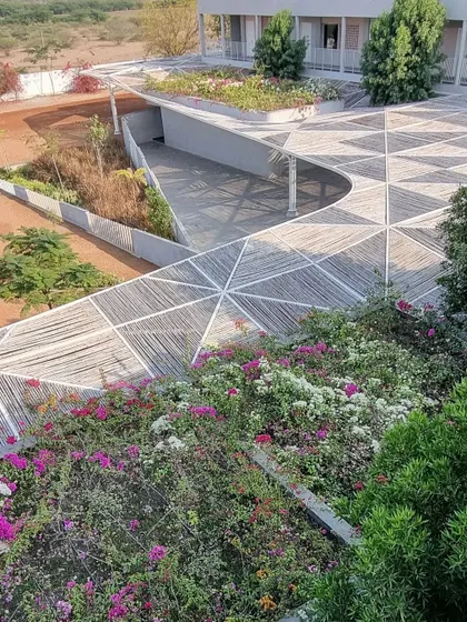 An aerial view of the completed Talaricheruvu Rural School, showing how the geometric bamboo canopy flows over the landscape. The rooftop is covered in bougainvillea, integrating the building with its natural surroundings.