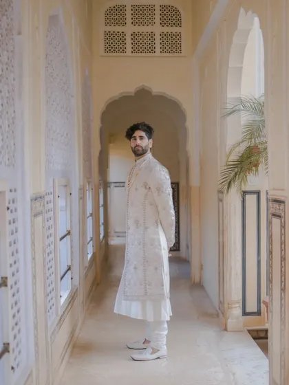 The groom strikes a pose in a sunlit palace corridor, the natural light and architecture creating a serene and timeless portrait.