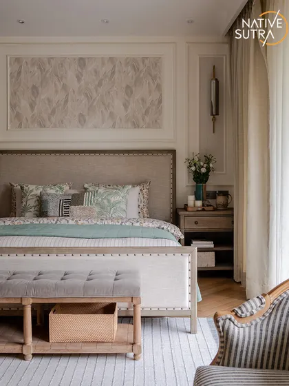 Another angle of the classic-meets-rustic master bedroom. The striped rug and armchair complement the neutral palette, while the large window and sheer curtains maintain a light and airy feel.