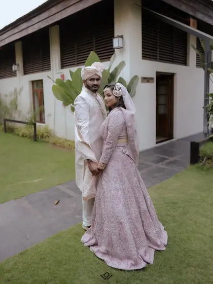 A full-length portrait of a Muslim couple in their wedding attire, posing in a garden.