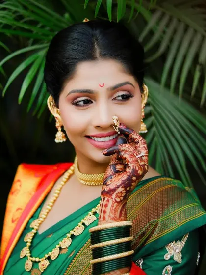 A classic bridal portrait of a Maharashtrian bride. She touches her traditional nath, drawing attention to her intricate jewelry and the beautiful mehndi on her hand.