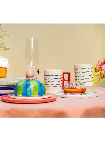 A close-up of a quirky, colorful tablescape, with a hand reaching for a modern mug. This shot highlights the unique design of the products.