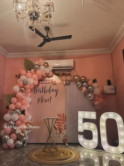A full view of the elegant 50th birthday decor we created for a client's mom. The setup includes a custom arch backdrop, a pink and rose gold balloon garland, and a large '50' marquee sign.