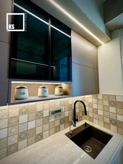 The sink area features a modern black faucet that complements the dark accents in the cabinetry and backsplash. The under-mount sink provides a seamless and easy-to-clean counter surface.