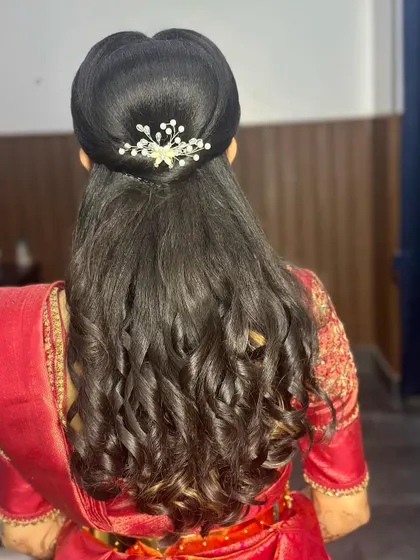 A classic reception hairstyle with defined curls and a half-updo, adorned with a small, sparkling pearl accessory.