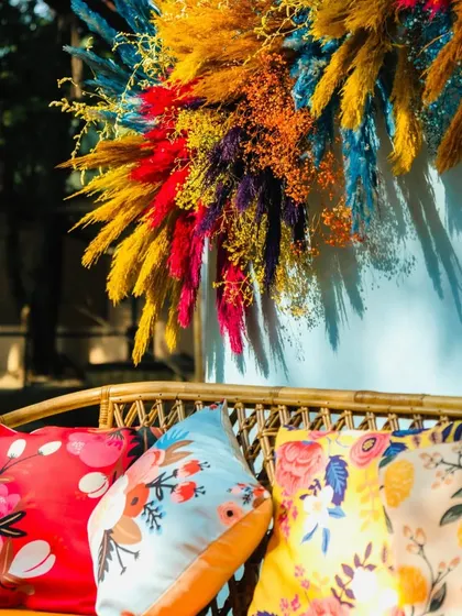 A stylish seating nook with a cane bench, colorful printed cushions, and a vibrant pampas grass arrangement on the wall.