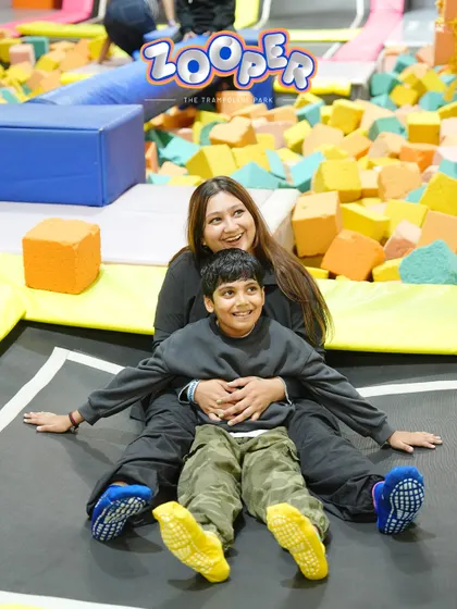 A mother and son share a smile while sitting on a trampoline surrounded by foam blocks. It's all about making memories together.