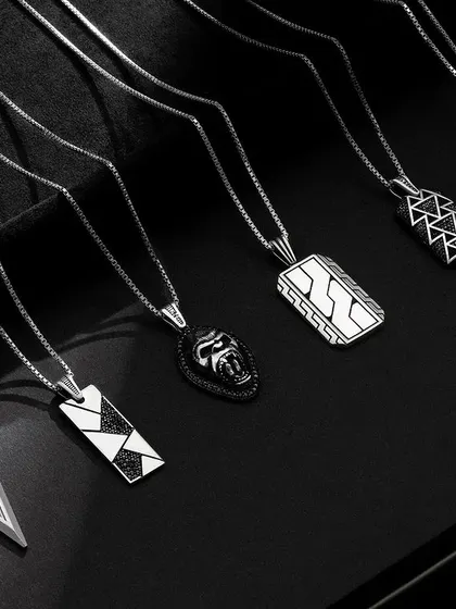 A dynamic arrangement of men's necklaces from Orionz Jewels. The pieces are laid out to showcase their unique designs, with moody lighting enhancing their metallic sheen against the dark backdrop.