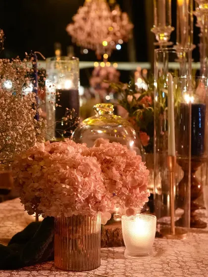 A detailed shot focusing on a simple arrangement of pink hydrangeas in a metallic vase, surrounded by candlelight. This shows that even smaller elements of our designs are crafted with care and elegance.