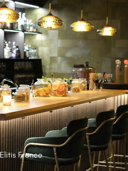 In this bar setting, a textured wallcovering from Élitis France adds a layer of timeless elegance. The subtle pattern complements the warm lighting and rich materials, contributing to an atmosphere of pure opulence.