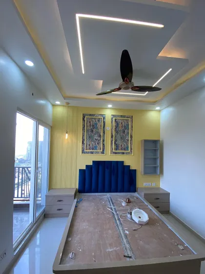 A wide shot of the master bedroom before the mattress is placed, showing the complete layout including the bed, side tables, and window.