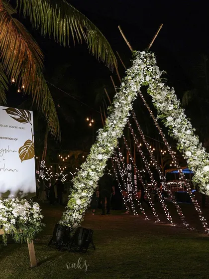 The welcome area for a starlit beach reception. A modern welcome sign stands next to the magnificent teepee arch, inviting guests into an evening of celebration.
