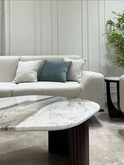 A close-up of a custom living room set. The organic shape of the Italian stone coffee table contrasts beautifully with the clean lines of the sofa and the fluted texture of the table's base.