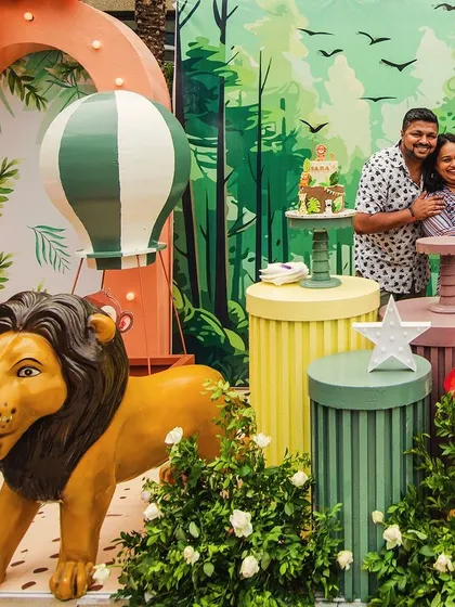 A happy family portrait at Sara's 'Wild Two' celebration. The colorful and friendly jungle backdrop, complete with a lion, hot air balloon, and mushroom props, creates a fun and memorable photo spot.