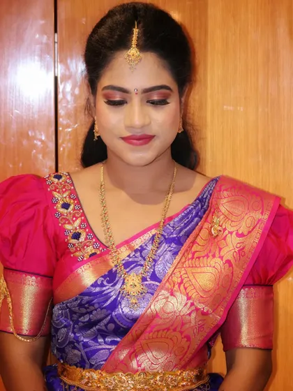 A classic look for the groom's sister, featuring a subtle smokey eye and a pink lip that complements her purple and pink silk saree.