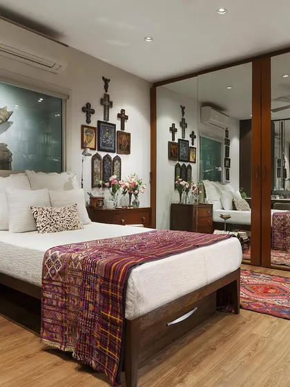 The bedroom in the Courtyard Home, with mirrored wardrobe doors that reflect the room and enhance the sense of space. The design is a harmonious blend of personal art, antique textiles, and functional storage.