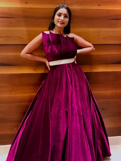 A full-length shot of the magenta velvet gown against a modern wooden backdrop. The pleated bodice and silver belt add a touch of contemporary design to this classic silhouette.