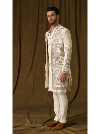 A side profile of the 'Pragyan' ivory shrug set, offering a clear view of the sleeve embroidery and the clean lines of the cigarette trousers. This angle highlights the tailored fit that is crucial to my work.