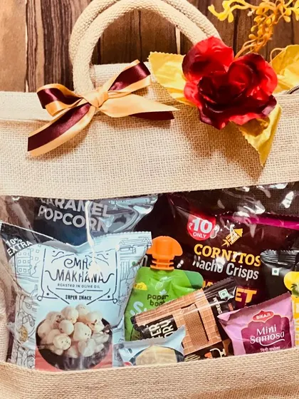 A detailed shot of a single wedding room hamper. The jute bag is filled with a variety of snacks like popcorn, makhana, and nacho crisps.