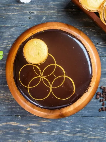 An elegant Dark Chocolate Fantasy cake, decorated with a golden macaron and a beautiful hand-drawn pattern. This premium cake is perfect for special occasions like Mother's Day.