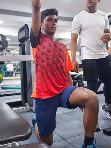 A coach assists a player with a single-arm dumbbell press, an exercise that develops unilateral strength and stability for better racket control.