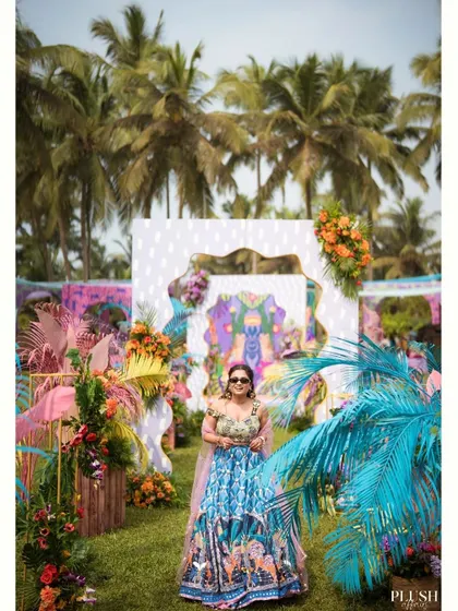 A guest poses against the vibrant, multi-layered photo booth I designed for a carnival-themed Mehendi in Goa. The backdrop includes quirky patterns, colorful florals, and even a flamingo.