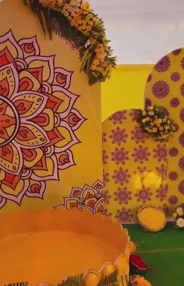 A close-up view of a custom Haldi ceremony backdrop. This design features hand-painted mandala art on a yellow panel, paired with marigold flower arrangements and a traditional urli for the ceremony.