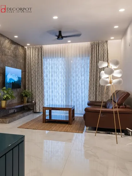 A contemporary living room featuring a unique TV unit against a textured stone wall. The space is furnished with a comfortable leather recliner and a modern floor lamp, creating a perfect spot for relaxation.