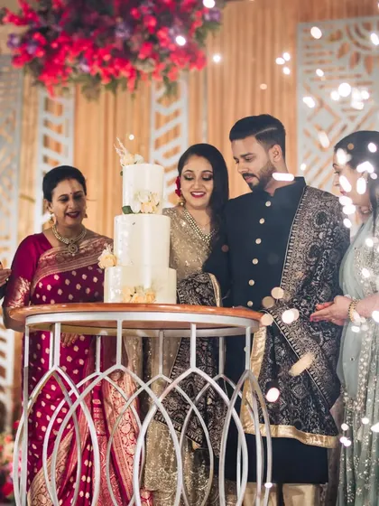 The cake cutting ceremony surrounded by family. The elegant stage decor, with its warm lighting and floral arrangements, provides a beautiful setting for this key reception moment.