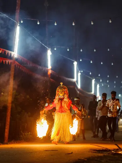 A powerful shot of a Bhoota Kola performer with two large torches, the flames illuminating the smoke-filled path. My low-light photography skills are essential for capturing the raw, spiritual energy of these sacred events.
