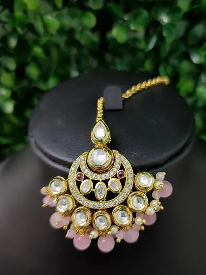 A pretty crescent-shaped maang tikka with kundan work and soft pink bead drops. Perfect for a pastel-themed wedding look.