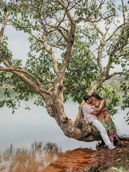 Finding a quiet moment together under a sprawling tree by the water. This wide shot shows the beautiful, peaceful setting for their love story.