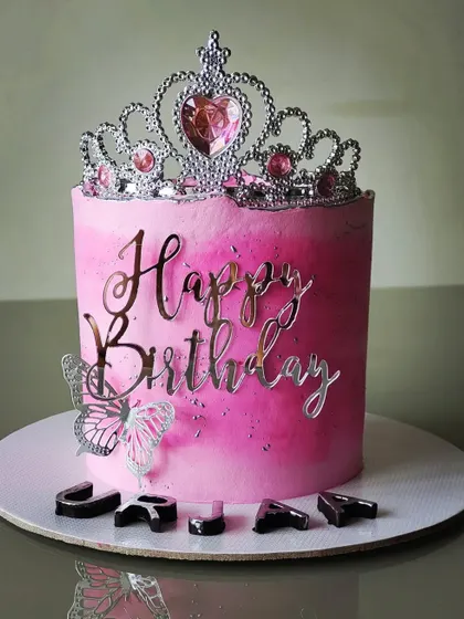 A pretty-in-pink birthday cake for a princess. The design features a pink ombre buttercream, a silver tiara, and a "Happy Birthday" topper for a fun yet elegant celebration.