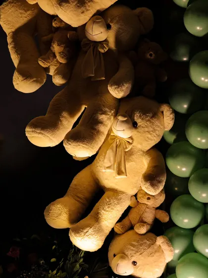 A whimsical installation of teddy bears appears to be climbing a wall next to a column of green balloons. This playful and eye-catching decor element was a favorite among both children and adults at the party.