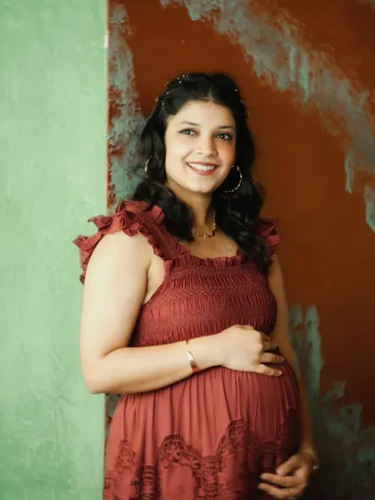 A glowing portrait of a mother-to-be in a rustic-themed indoor setting. The textured wall and her happy expression make for a beautiful, warm image.