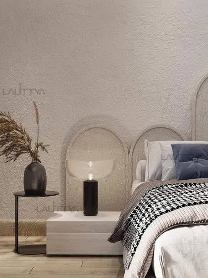A detail of a modern, minimalist bed design. The neutral-toned headboard with an arched design creates a soft backdrop, complemented by a houndstooth throw and a simple black side table.
